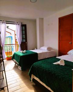 a bedroom with two beds with green sheets and a window at Hotel Casa Helena in Filandia
