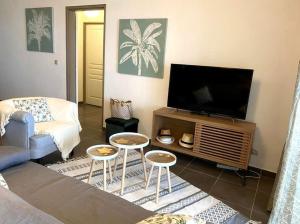 ein Wohnzimmer mit einem Flachbild-TV und 2 Tischen in der Unterkunft Appartement de standing, vue mer à 5mn du lagon in Saint-Paul