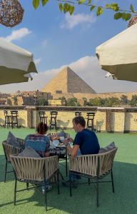 Un uomo e una donna seduti a un tavolo di fronte alla piramide. di Master Pyramids Inn a Il Cairo