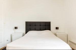 een wit bed met een zwart hoofdeinde in een slaapkamer bij Le Gandhy 2 in Le Blanc-Mesnil