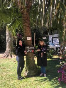 dos mujeres de pie junto a un árbol con una señal en Vó Janete Haus, en Gramado