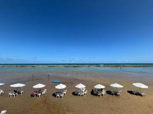 a beach with tables and chairs and white umbrellas at Ekoara Residence in Porto De Galinhas