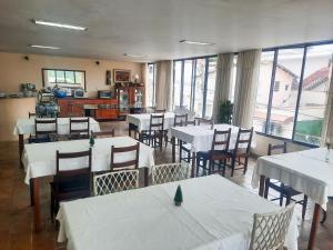 a dining room with white tables and chairs and windows at Hotel Pousada das Rosas in São Lourenço