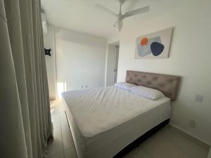 um pequeno quarto branco com uma cama e uma ventoinha de tecto em Village blue AC Wi-Fi piscina em Cabo Frio