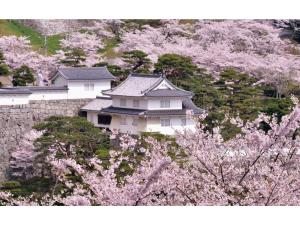 ein weißes Gebäude mit akura-Bäumen vor einer Burg in der Unterkunft Urban Hotel Nihonmatsu - Vacation STAY 78339v in Nihommatsu