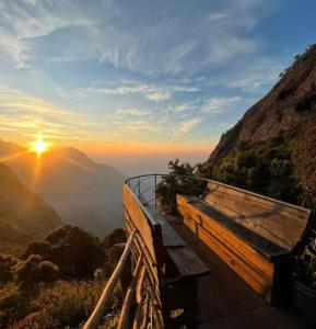 a bench on top of a mountain with the sunset at Munnar green portico cottage in Munnar