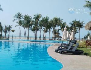 a swimming pool with chairs and palm trees at Encanto de Depa c/ Alberca y Club de Playa Privado in Barra Vieja