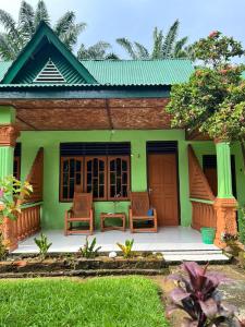 una casa verde con 2 sillas y una mesa en Wisma Batu Mandi and offers jungle tours en Bukit Lawang
