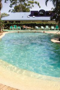 a large pool of blue water with chairs and tables at Smugglers Cove Holiday Village in Forster