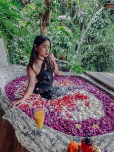 Ein junges Mädchen sitzt in einem Blumenpool mit einem Brunnen. in der Unterkunft Bali Inang Jungle View in Tampaksiring