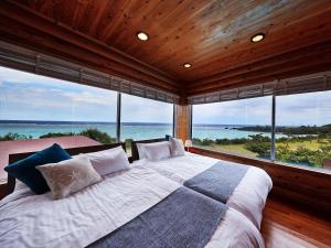 um quarto com uma cama grande e janelas grandes em Nagahama Beach Resort Kanon em Nakijin