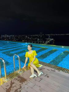 a woman in a yellow dress sitting next to a swimming pool at Luxury Ocean View Danang Golden Bay in Danang