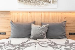 a bed with grey pillows and a wooden wall at Lienbichl in Saalbach Hinterglemm