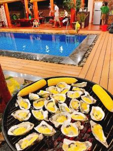 a grill with oysters and corn next to a swimming pool at THE LAND OF LOVE Homestay - Venuestay in Dak Lak