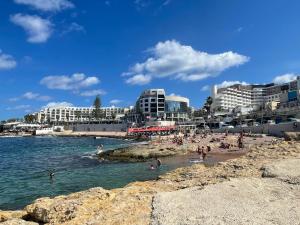 a beach with people in the water and buildings at DoMiSol duplex suites near sea in St. Paul's Bay