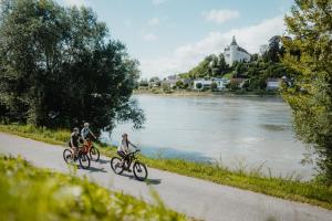Tres personas en bicicleta por un camino junto a un río en Privatzimmer - Sieben an der Donau en Ottensheim