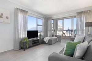 a living room with a couch and a tv and some windows at Ocean View 503 in Bloubergstrand