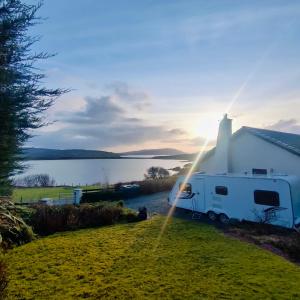 a white caravan parked next to a white house with the sun setting at Kintyre Caravan in Portree
