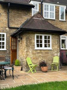 twee groene stoelen en een tafel voor een bakstenen huis bij The Hidden Cottage in Londen