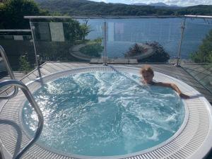 een persoon in een jacuzzi met uitzicht op het water bij The Penthouse Bowness Luxury Loft Jacuzzi Bath & Complimentary Lakeview Spa Membership in Bowness-on-Windermere