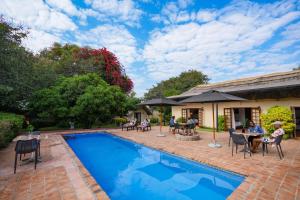 una piscina con personas sentadas alrededor de mesas y sillas junto a una casa en The Little Outlook en Victoria Falls