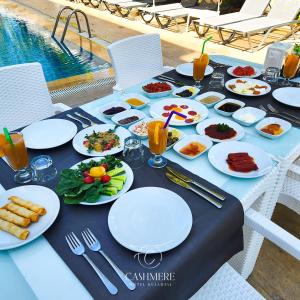 une table avec des assiettes de nourriture sur une table près d'une piscine dans l'établissement Cashmere Hotel, à Kusadası