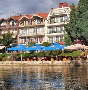 a hotel with blue umbrellas and chairs next to the water at Struga Riverview Hotel in Struga