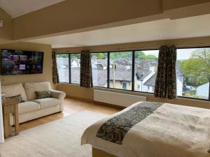 a bedroom with a bed and a couch and windows at The Penthouse Bowness Luxury Loft Jacuzzi Bath & Complimentary Lakeview Spa Membership in Bowness-on-Windermere