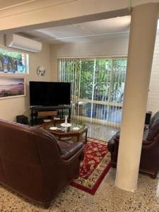 a living room with leather furniture and a large television at The singing frogs studio in Coffs Harbour