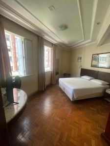 um quarto com uma cama, uma mesa e janelas em Brasil Palace Hotel em Belo Horizonte