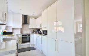 Addlestone Stylish Spacious Three Bedroom House في آدلستون: مطبخ أبيض مع خزائن بيضاء وأجهزة