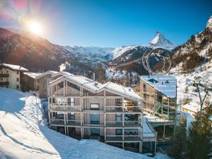 um edifício na neve com as montanhas ao fundo em Matterhorn FOCUS Design Hotel em Zermatt