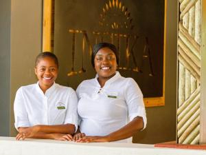 two women in white shirts standing next to a table at Insika lodge in Victoria Falls