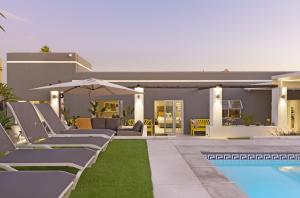 a pool with lounge chairs and an umbrella next to a house at Rancho Relaxo in Bloubergstrand