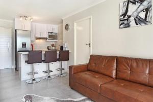sala de estar con sofá marrón y cocina en The Paragon 317 by HostAgents, en Ciudad del Cabo