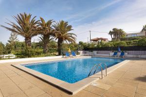 a swimming pool with blue chairs and palm trees at Alto da Praia Villa in Colares