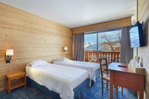 ラルプ・デュエズにあるオテル エリオヴァ ル シェのベッド2台、デスク、窓が備わるホテルルームです。
