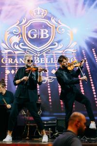 Zwei Männer spielen Violinen auf einer Bühne mit einem Orchester in der Unterkunft Grand Bellagio Batumi Convention & Casino Hotel in Batumi