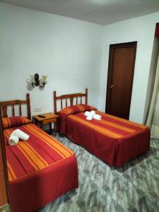 two beds in a hotel room with red sheets at Pension Rioja in Quinto