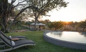 a pool with two benches next to a park with the sunset at Kolokolo Safari Home in Lentswelemoriti