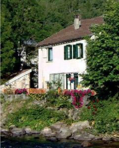 ein weißes Haus mit grünen Fenstern und Blumen davor in der Unterkunft Gîte du petit Taïchou in Luzenac