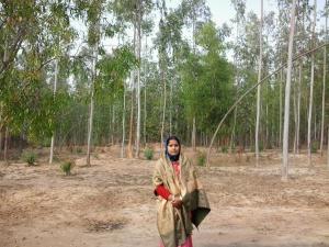 a woman standing in a field with trees in the background at RAJ MAHAL GUEST HOUSE in Shānti Niketan