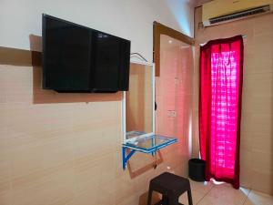een flatscreen-tv aan een muur met een rood gordijn bij OYO 93278 Wisma Syariah Lahundape in Kendari
