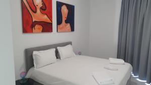 a bedroom with a white bed with three paintings on the wall at Hypnos Residence in Nicosia