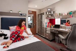 Una chica sentada en una cama en una habitación con escritorio en For Students Only Studios and Ensuite Bedrooms with Shared Kitchen at Talbot Street in Nottingham, en Nottingham