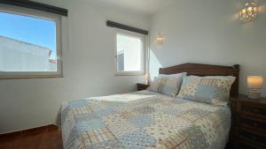 a bedroom with a bed with a quilt and two windows at Apartamento Miradouro in Carrapateira