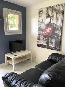a living room with a black leather couch and a tv at Studio cosy indépendant avec Jardin à Osny proche Cergy pontoise in Osny