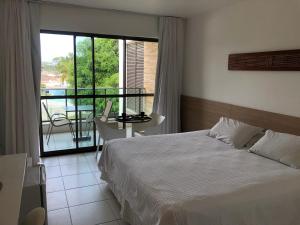 a bedroom with a bed and a balcony with a table at Iloa Flat Barra São Miguel-Alagoas in Barra de São Miguel