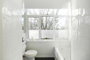 biała łazienka z toaletą, wanną i oknem w obiekcie The Putney Hideout - Bright 1BDR Flat w Londynie