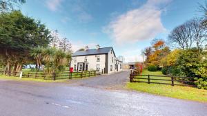 a white house with a fence next to a road at The Old Post Office Lodge in Enniskillen